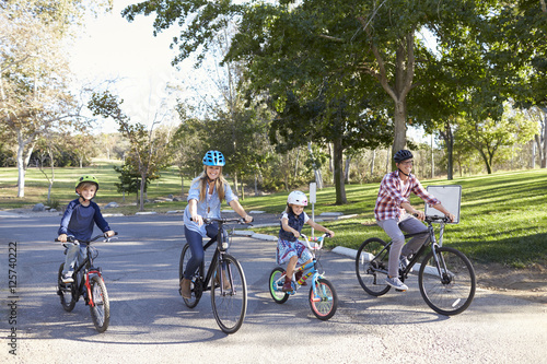 Young white family cycling together through a park