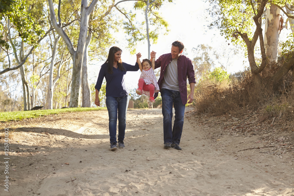 Couple walking on rural path lifting daughter, full length