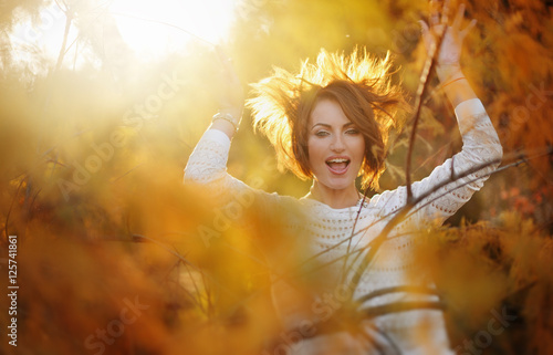 Молодая красивая девушка с короткой стрижкой смеется среди деревьев на закате