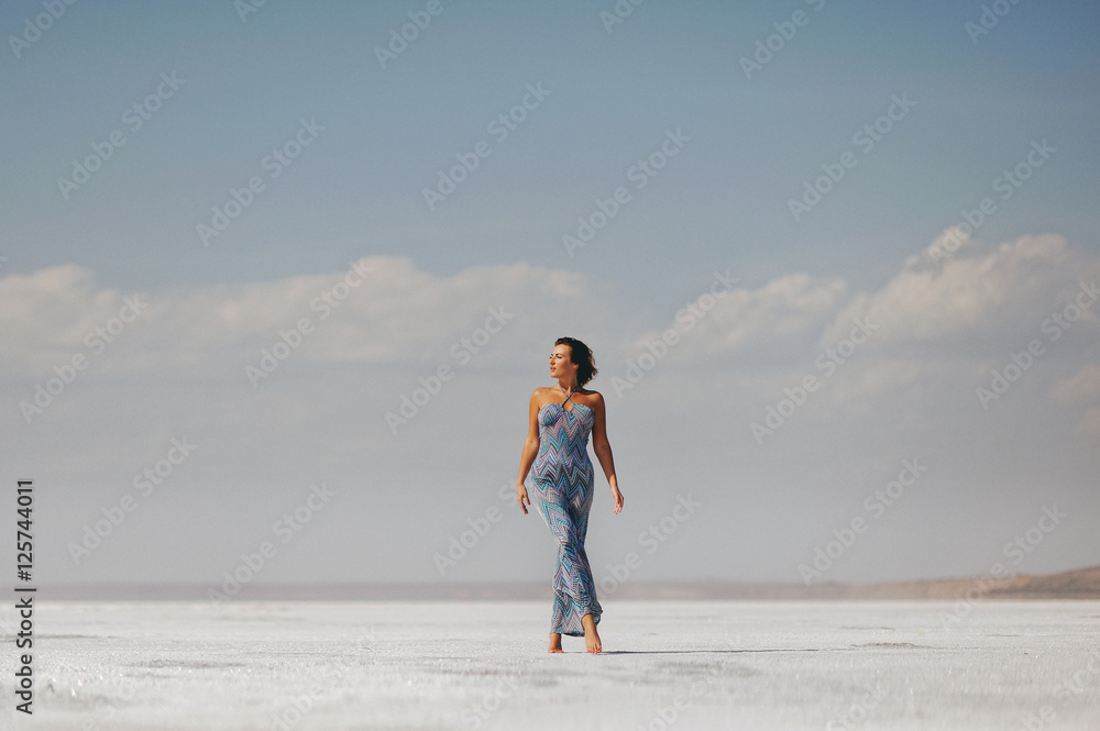 Молодая стройная женщина идет по  пустыне в длинном узком платье
