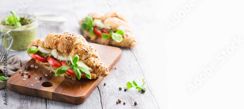Wholegrain croissants with mozzarella, tomato and pesto, white wooden background