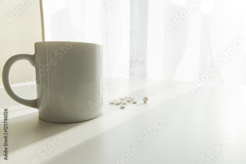 white pills lying next to a glass of water on a wooden table