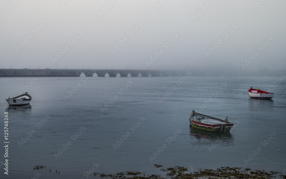 Barcas en la niebla al amanecer con puente al fondo formando triangulo