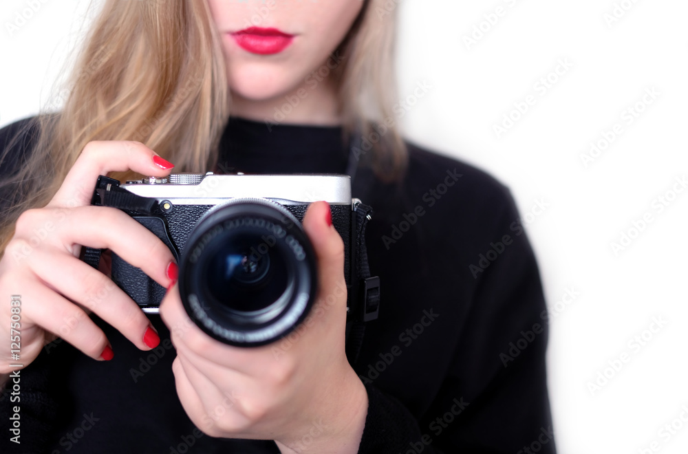 The girl photographer with blond hair in black shirt holds modern black color digital camera with lens pointing forward. Horizontal indoor studio photo close-up isolated on white with focus on camera The girl photographer with blond hair in black shirt holds modern black color digital camera with lens pointing forward. Horizontal indoor studio photo close-up isolated on white with focus on camera