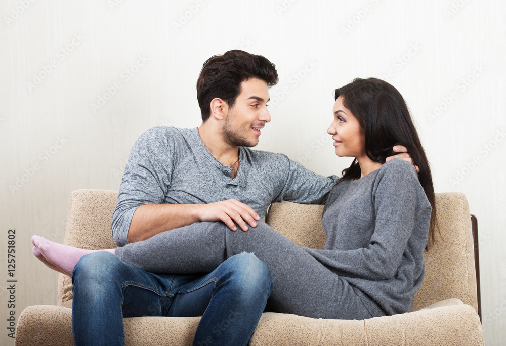 Young happy couple talking each other sitting on a sofa Young happy couple talking each other sitting on a sofa
