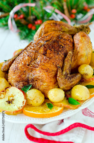 Christmas baked chicken (turkey) with oranges and apples on a wh