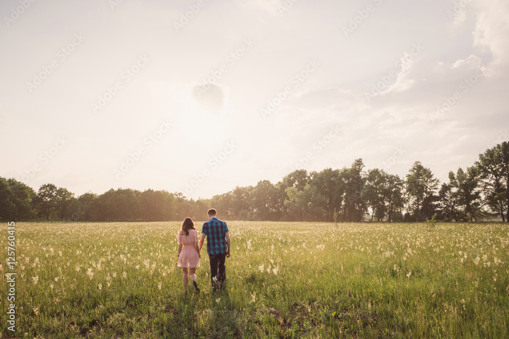 young couple walking in the field with flowers in sunlight