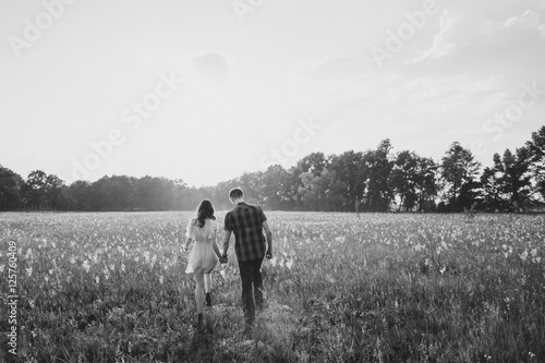 young couple walkind in the field with flowers in sunlight in black and white photo