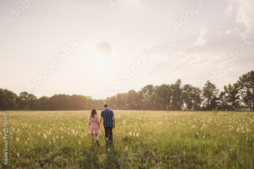 young couple walking in the field with flowers in sunlight