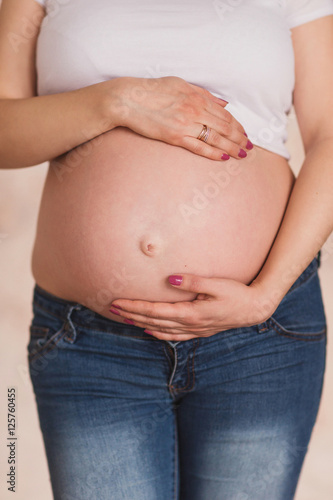 pregnant woman in jeans and white t-shirt holding her hands on her belly © anna_gorbenko