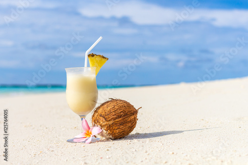 Pina Colada cocktail on the beach with coconut and exotic flower