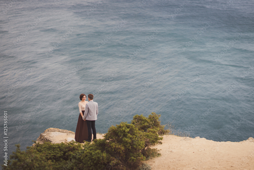 Romantic and stylish caucasian couple standing on the background of spectacular sea view. Love, relationships, romance, happiness concept. Romantic and stylish caucasian couple standing on the background of spectacular sea view. Love, relationships, romance, happiness concept.