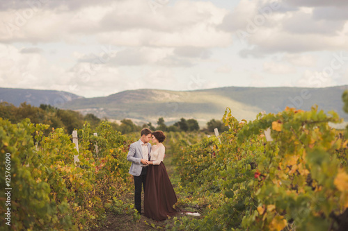 Romantic and stylish caucasian couple standing in the beautiful vineyard at sunset. Love, relationships, romance, happiness concept. © anna_gorbenko