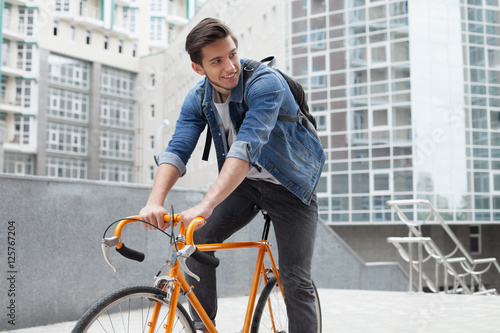 Fototapeta Naklejka Na Ścianę i Meble -  The guy goes to town on a bicycle in  blue jeans jacket .  young man  an orange fix bike