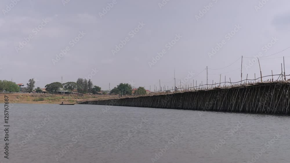 Long bamboo bridge and motorbikes crossing it. Fisherman rowing his small boat and passing under a bamboo bridge in the background Long bamboo bridge and motorbikes crossing it. Fisherman rowing his small boat and passing under a bamboo bridge in the background