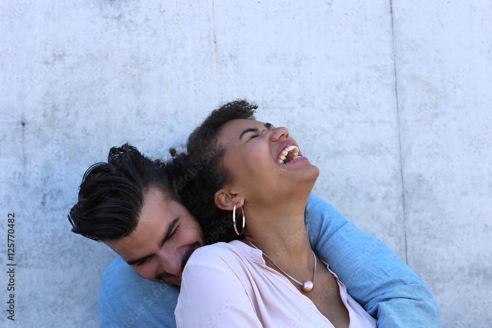 Attraktives Paar sitzt vor Beton Wand und lacht von Herzen