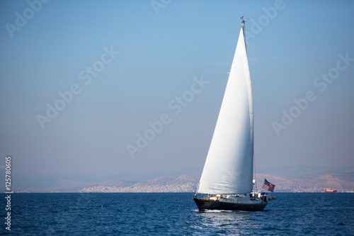 Sailing yacht with white sails in the fog in the sea near the coast.