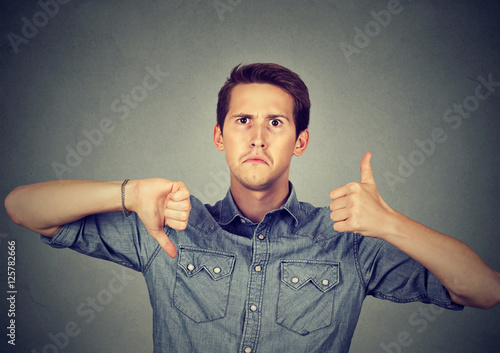 Vászonkép Perplexed man with thumbs down thumbs up gesture