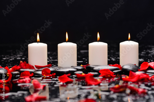 Many rose petals with four candle and therapy stones 