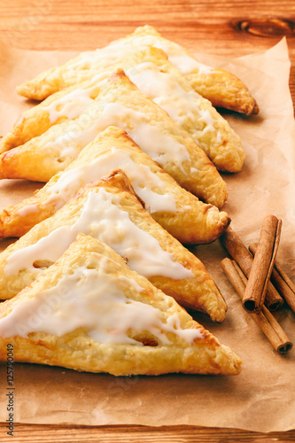 Puff pastries with apples and cinnamon on brown background.