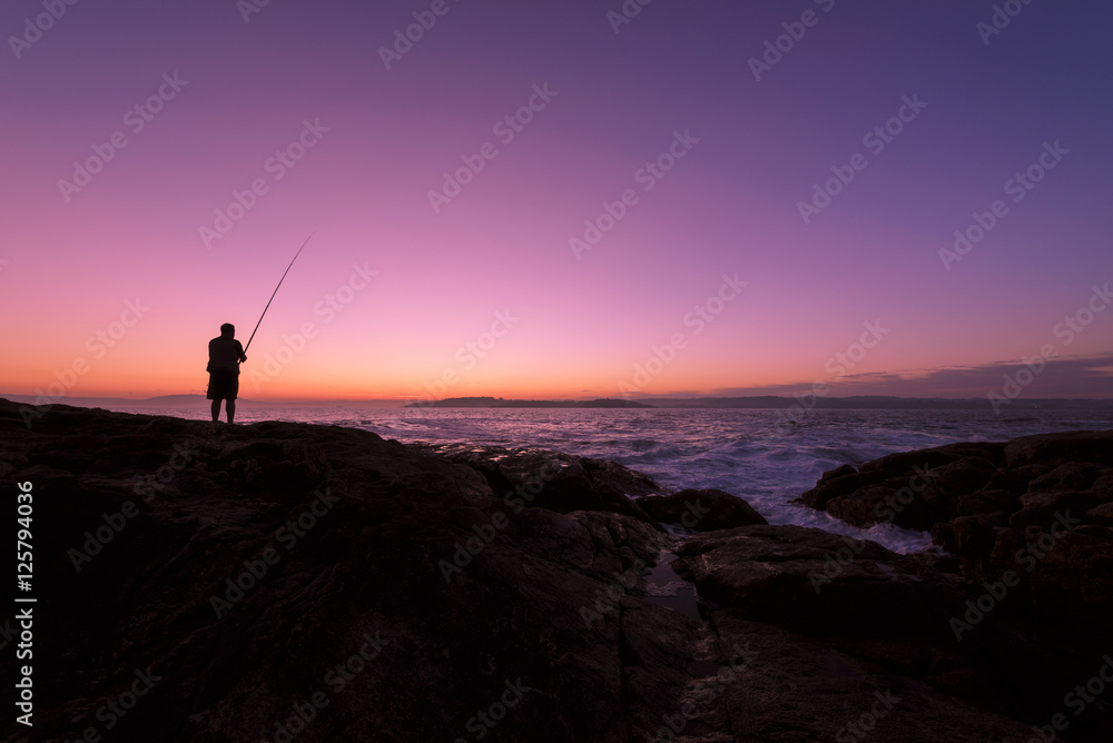 pescador a contraluz al amanecer con cielo multicolor