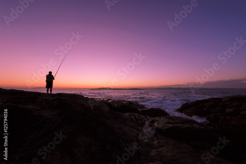 pescador a contraluz al amanecer con cielo multicolor