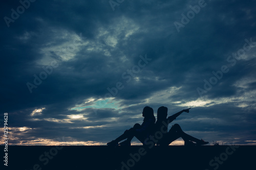 Silhouette of two women sitting lean