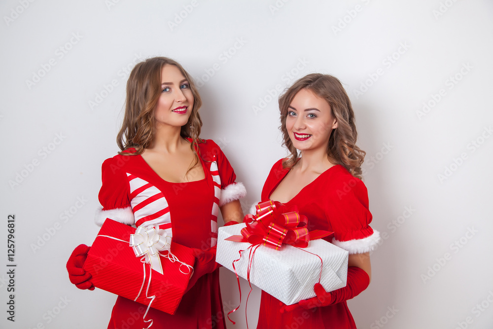 Beautiful happy two girls in Santa Claus clothes with a christmas gift Beautiful happy two girls in Santa Claus clothes with a christmas gift
