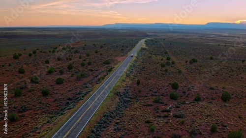 Picturesque and incredibly beautiful sweeping aerial of an RV driving into sunset on a highway in iconic Central US landscape in Utah, with dry  yellow grass flopping in the wind