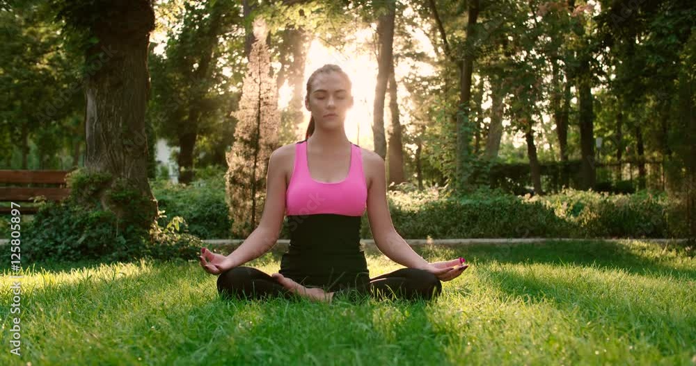 young beautiful Asian girl doing yoga in the Park in the Lotus position, Dolly shot, the glare of the sun young beautiful Asian girl doing yoga in the Park in the Lotus position, Dolly shot, the glare of the sun