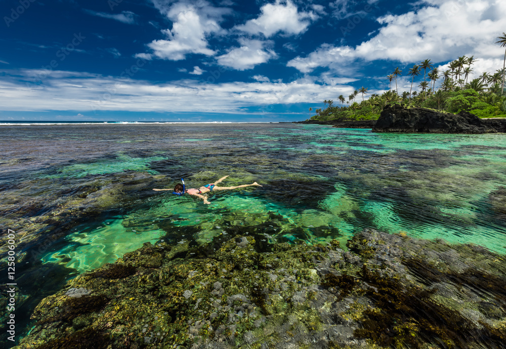 Young woman snorkeling over coral reef on a tropical island