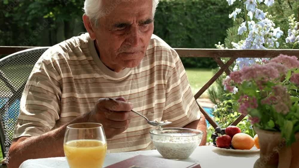 elderly man eats muesli at a table in a summer garden elderly man eats muesli at a table in a summer garden