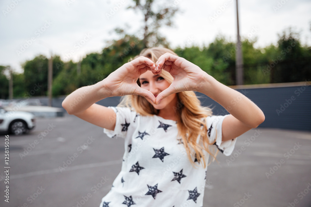 Smiling blonde woman making heart gesture with hands