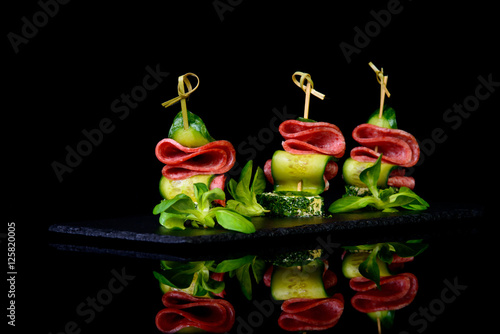 Bilde på lerret canape salami cucumber on black background with reflection