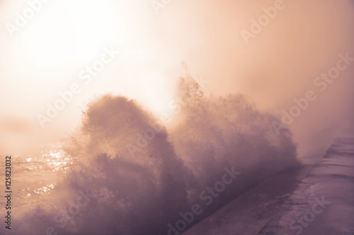 Wave slams into the breakwater in a misty day.