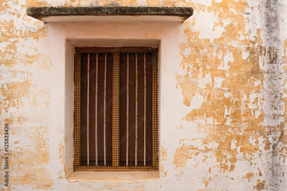 Fototapeta premium Vintage window on old wall - An old window with rusted protective mesh and rods on a old wall.