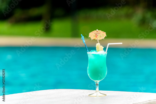 Glass of blue cocktail at swimming pool in summer time