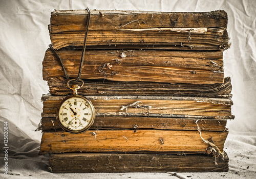 Pile of old dusty books with broken pocket watch on white cloth photo