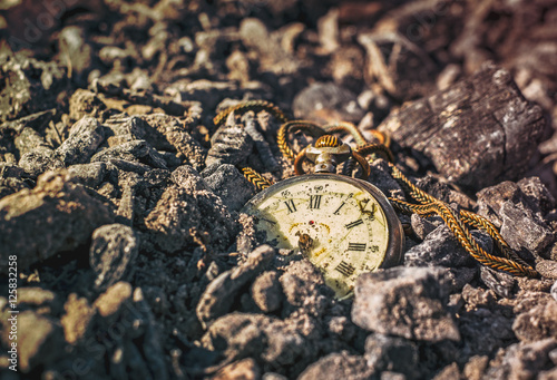 Still life with antique rotten pocket watch on ashes in the forest at the sunset