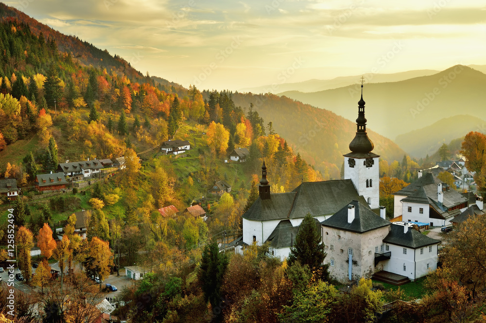 Fall in Slovakia. Old mining village. Historic church in Spania dolina. Autumn colored trees at sunset. - obrazy, fototapety, plakaty 