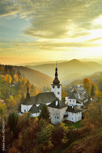 Fall in Slovakia. Old mining village. Historic church in Spania dolina. Autumn colored trees at sunset.