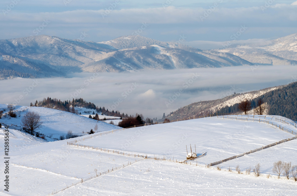 Fenced pastures in the mountains in the winter under the snow at sunrise. Winter mountain landscape.
