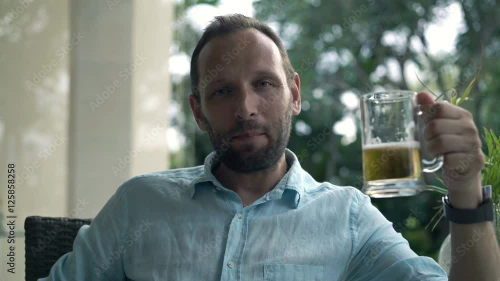 Happy, young man raising toast to camera and drinking beer in garden in cafe
Happy, young man raising toast to camera and drinking beer in garden in cafe