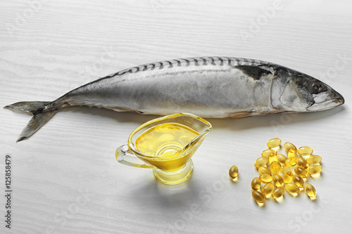 Fish oil pills and fresh fish on light background