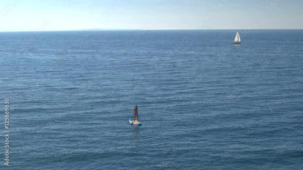 AERIAL: Happy young woman supping in crystal clear blue ocean on beautiful day AERIAL: Happy young woman supping in crystal clear blue ocean on beautiful day