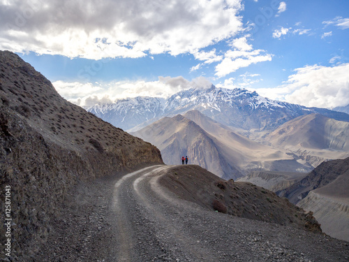 Two trekkers walking on the track road from the dark to the light with the snow mountain peak at distance as destination. Annapurna Conservation Area Nepal