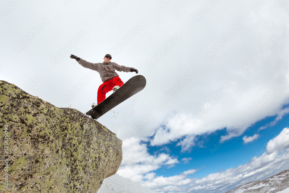 Snowboarder jumps from big rock Snowboarder jumps from big rock