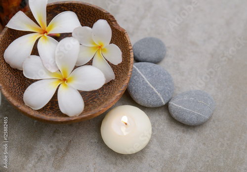 frangipani in wooden bowl with spa stones  candle on grey background.    