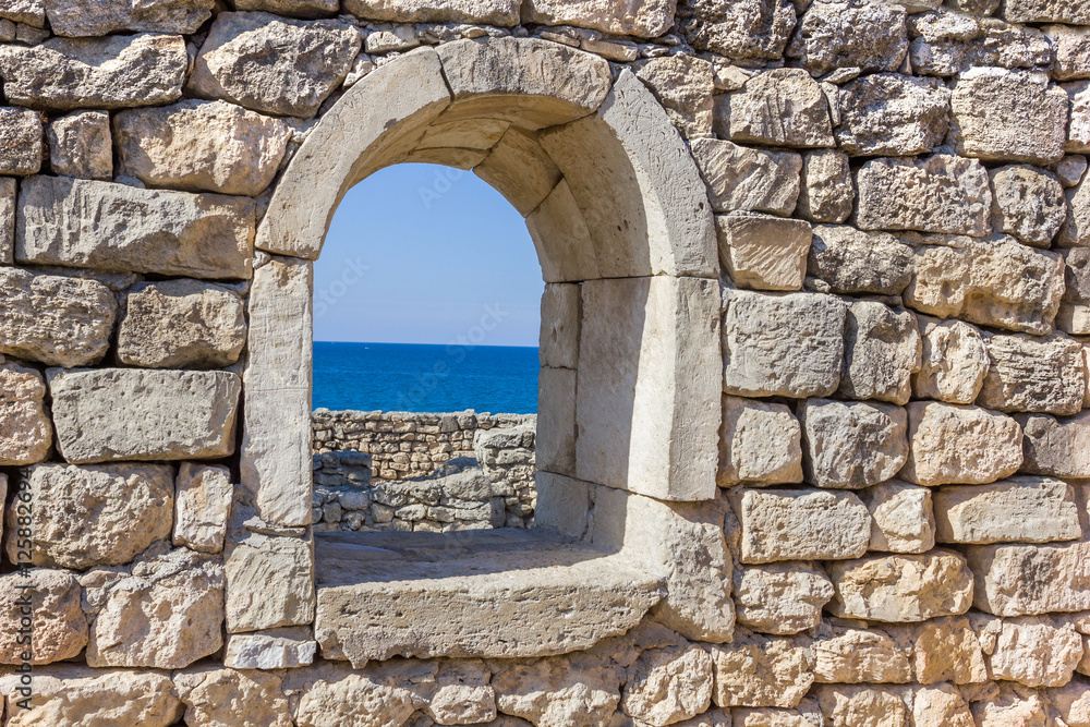 ancient stone wall with a window and a view of the sea