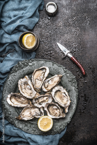 Open raw oysters on vintage plate with lemon and oysters knife, dark rustic background with water drops , top view